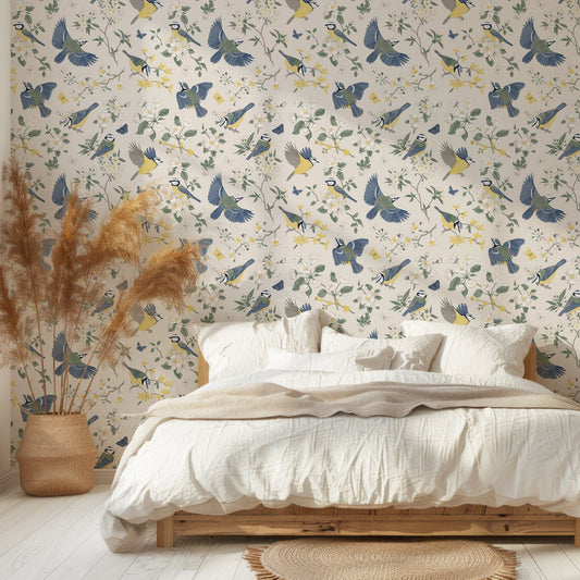 A bedroom with a palette framed bed with white bedding and pampas grass next to it featuring 'Adriana' which is a vintage wallpaper featuring colourful birds, butterflies, blooming flowers and leafy branches in an elegant Chinoiserie-inspired repeating botanical pattern.