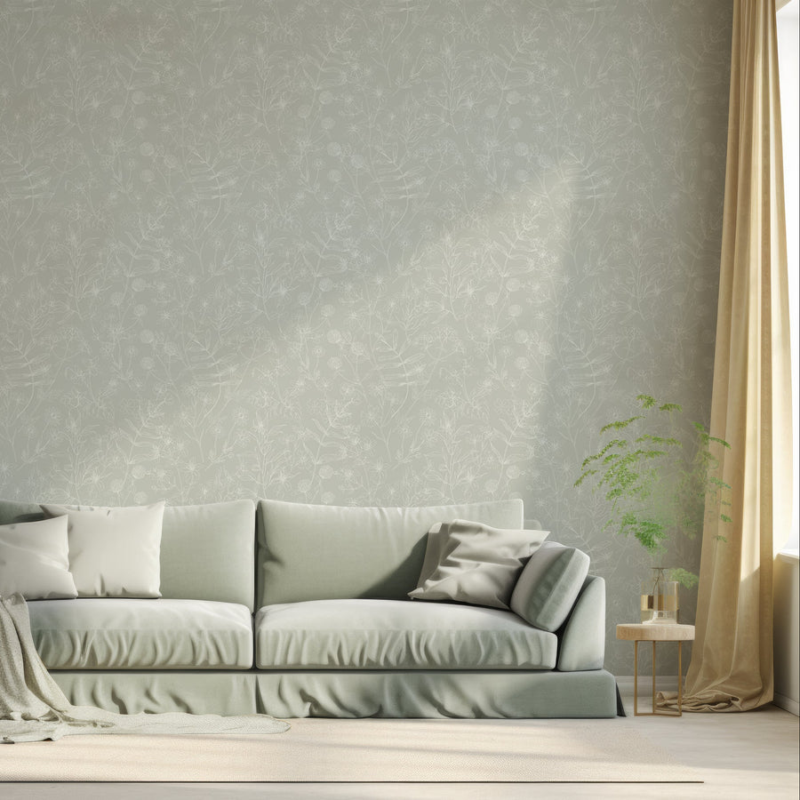 A living room with a light sage coloured sofa showing 'Blaire' which is a sage green wallpaper featuring delicate white botanical outlines of flowers, leaves and plants in an intricate repeating pattern.