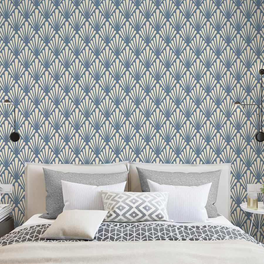 A bedroom showing a bed with white bedding with pillows and lights next to it featuring 'Virginia Slate' which is a slate grey Art Deco wallpaper featuring stylised geometric leaf fans and angular botanical motifs in a vintage-inspired repeating pattern.